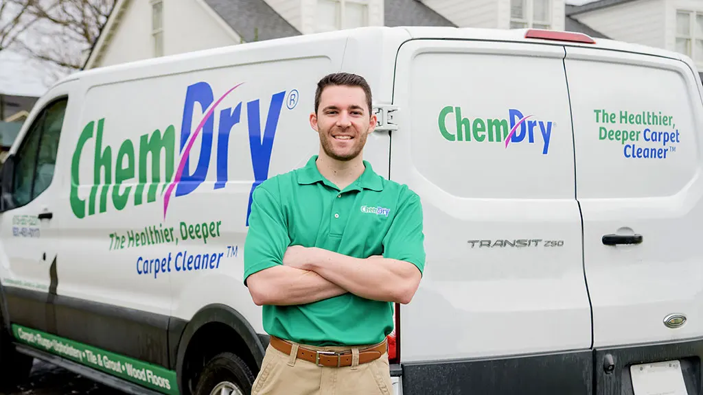 A smiling Chem-Dry technician in a green Chem-Dry polo, arms crossed, standing in front of a white Chem-Dry service van