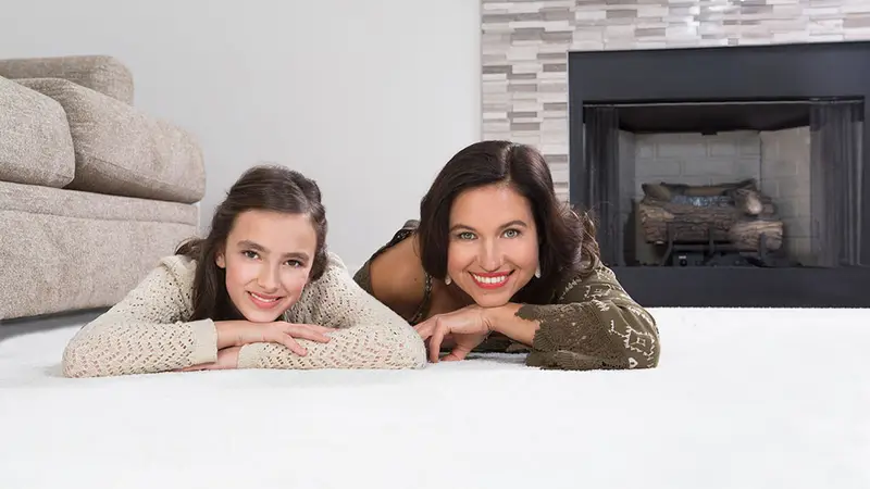 A mother and daughter lying on a clean white carpet, smiling